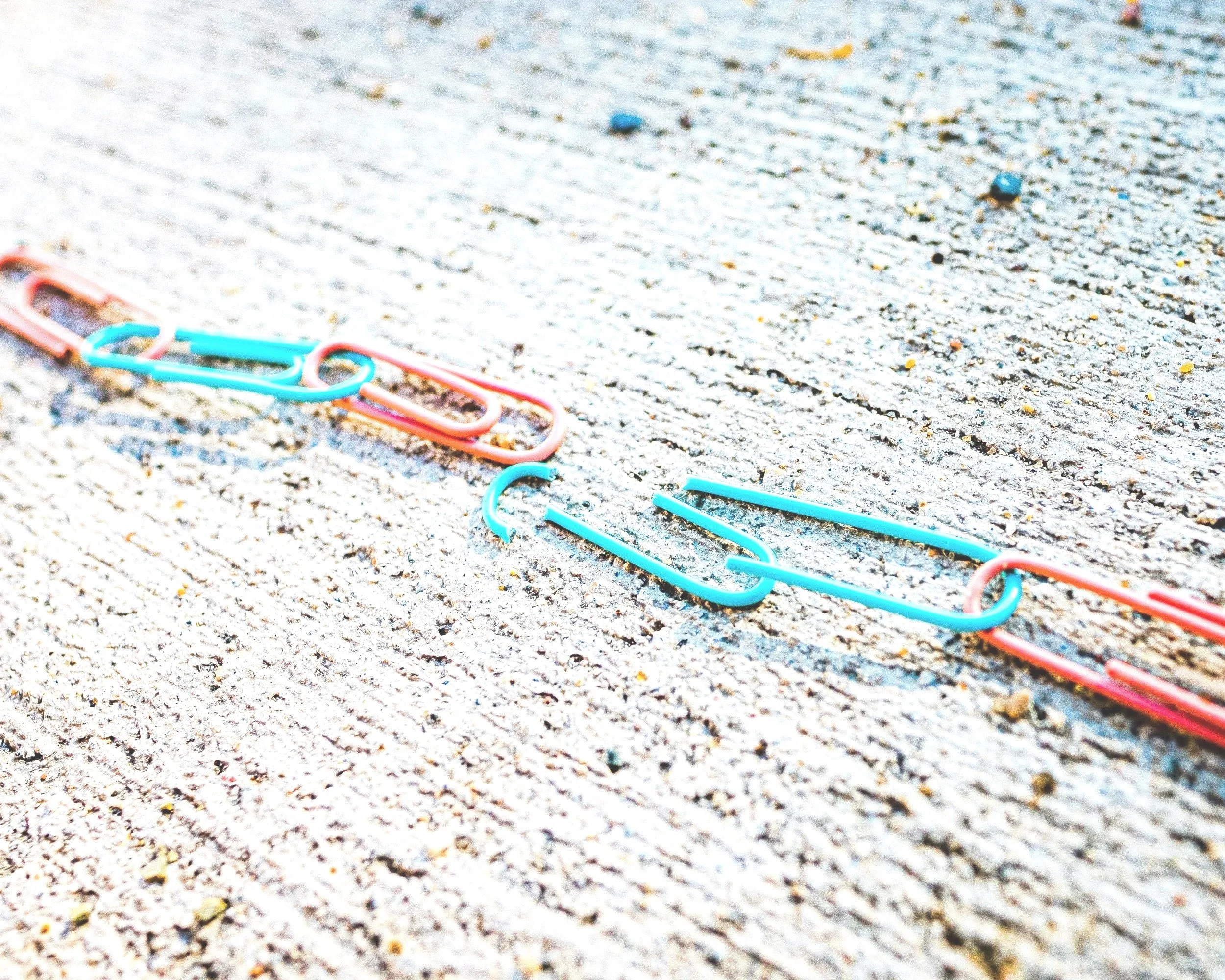 Colorful paperclips scattered on a wooden surface, with some connected to form a chain.