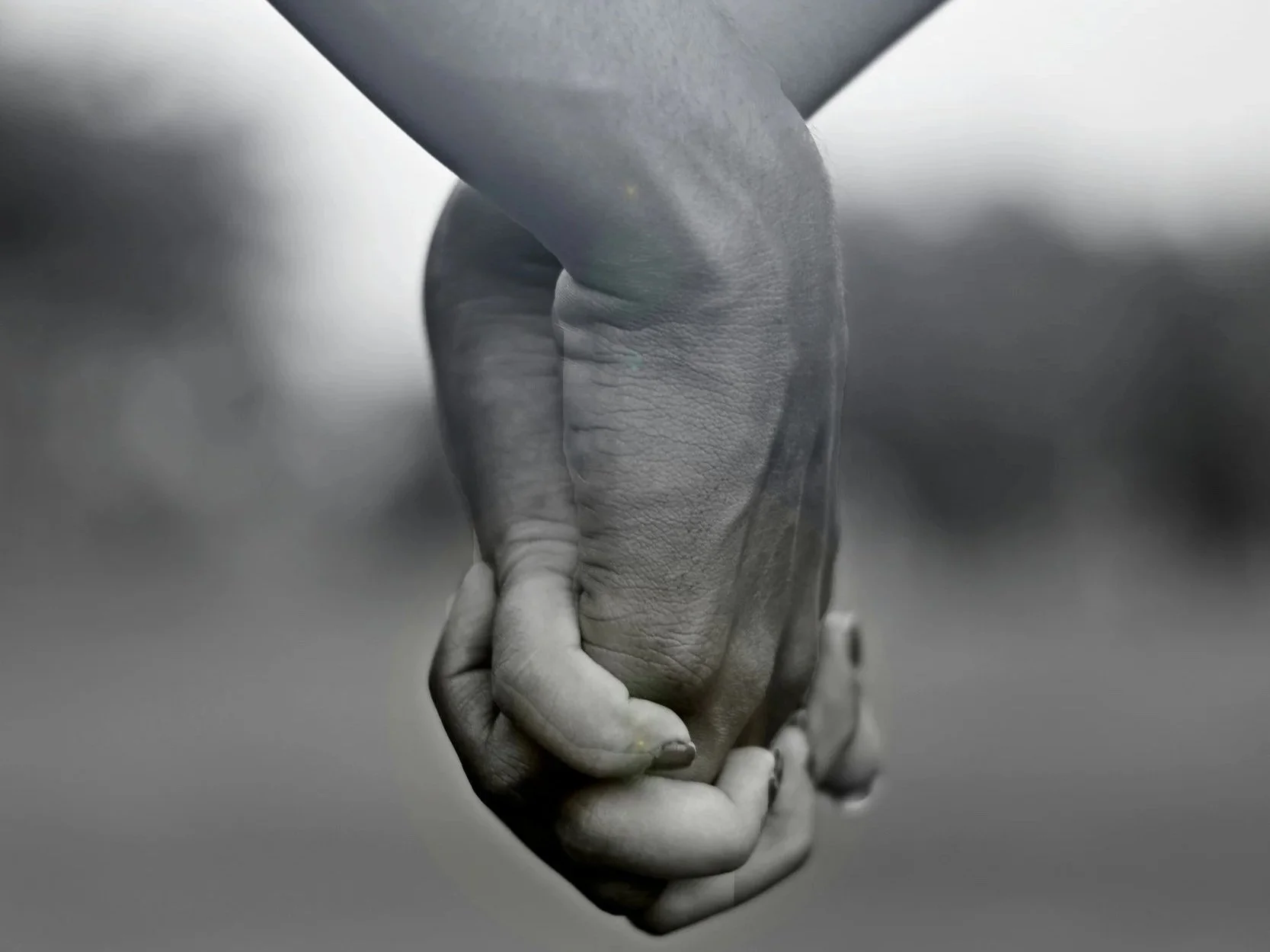 Close-up of a couple holding hands against a blurred outdoor background, symbolizing connection and support.