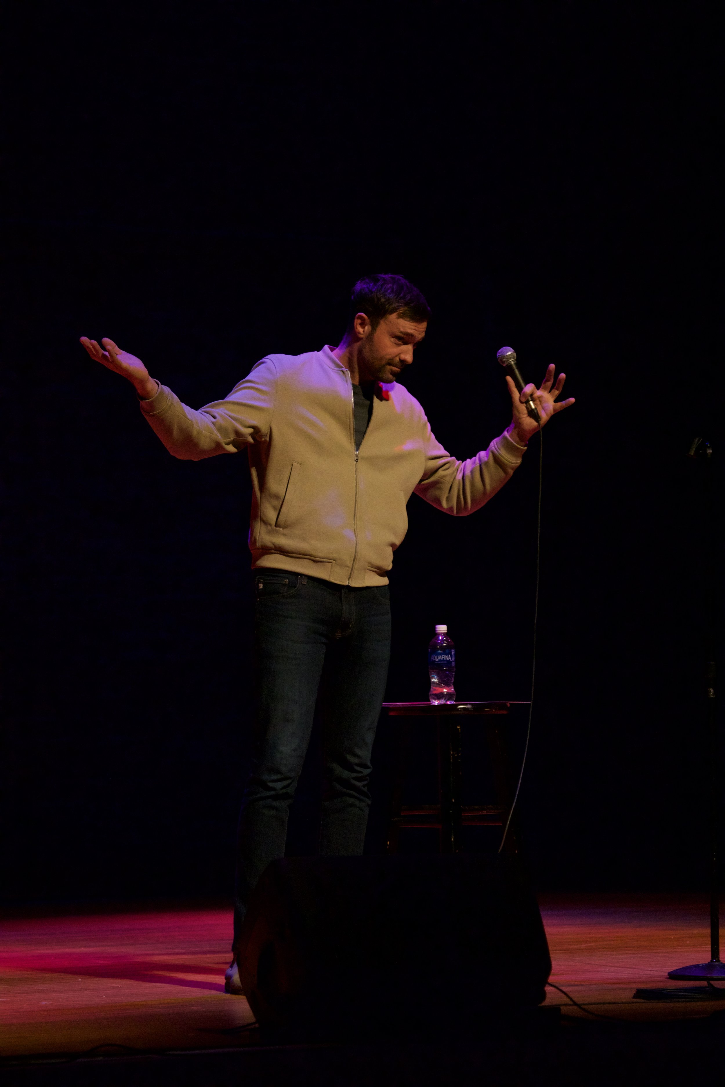 Photo of comedian Jeff Dye performing a live event during his tour, The Last Cowboy in L.A. He has his arms out wide in the air as he tells a joke.