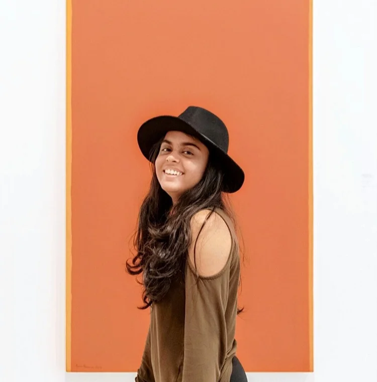 Aarushi Shah smiling in a black hat in front of an orange wall