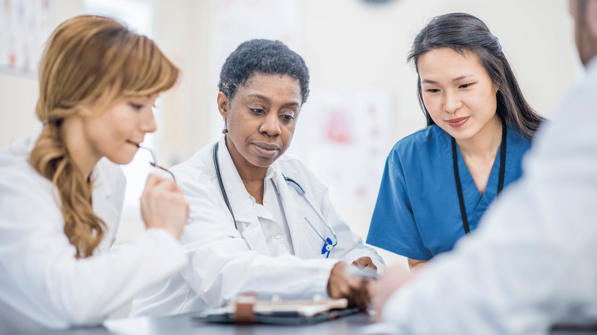Two female doctors and one female nurse look over documents on the table in front of them.