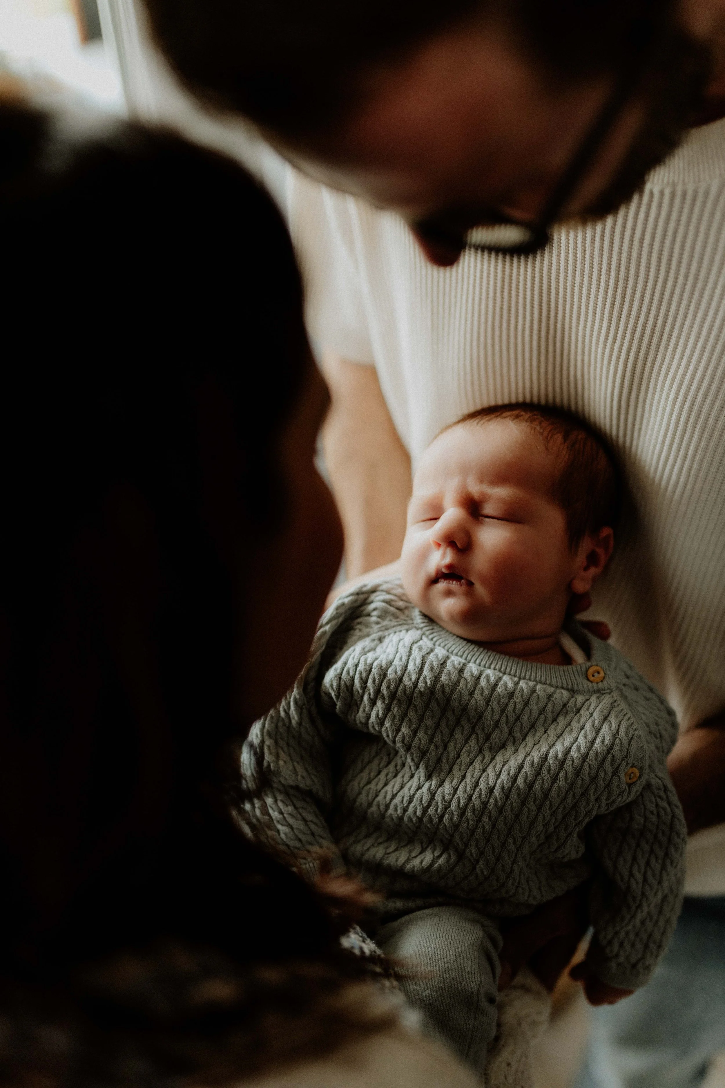 Békésen alvó újszülött baba egy felnőtt karjában, szemben egy hosszú sötét hajú nővel, feltehetően az édesanyával.