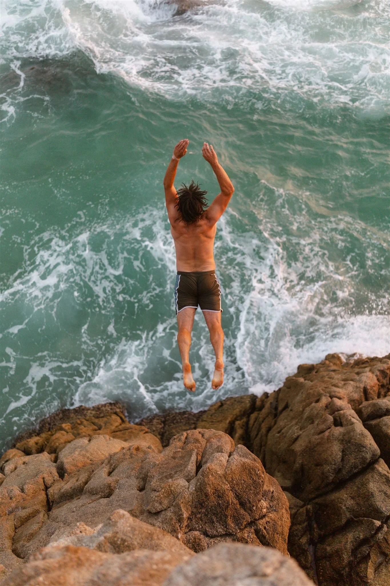A man jumping off a rocky cliff into the ocean.