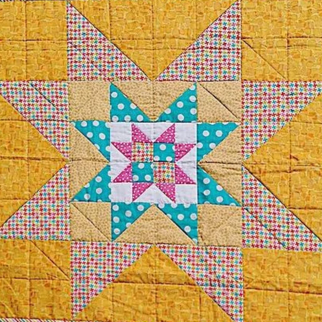 Close-up of a colorful quilt with a central star pattern surrounded by various patterned fabric squares and triangles, in colors including pink, blue, white, and yellow.