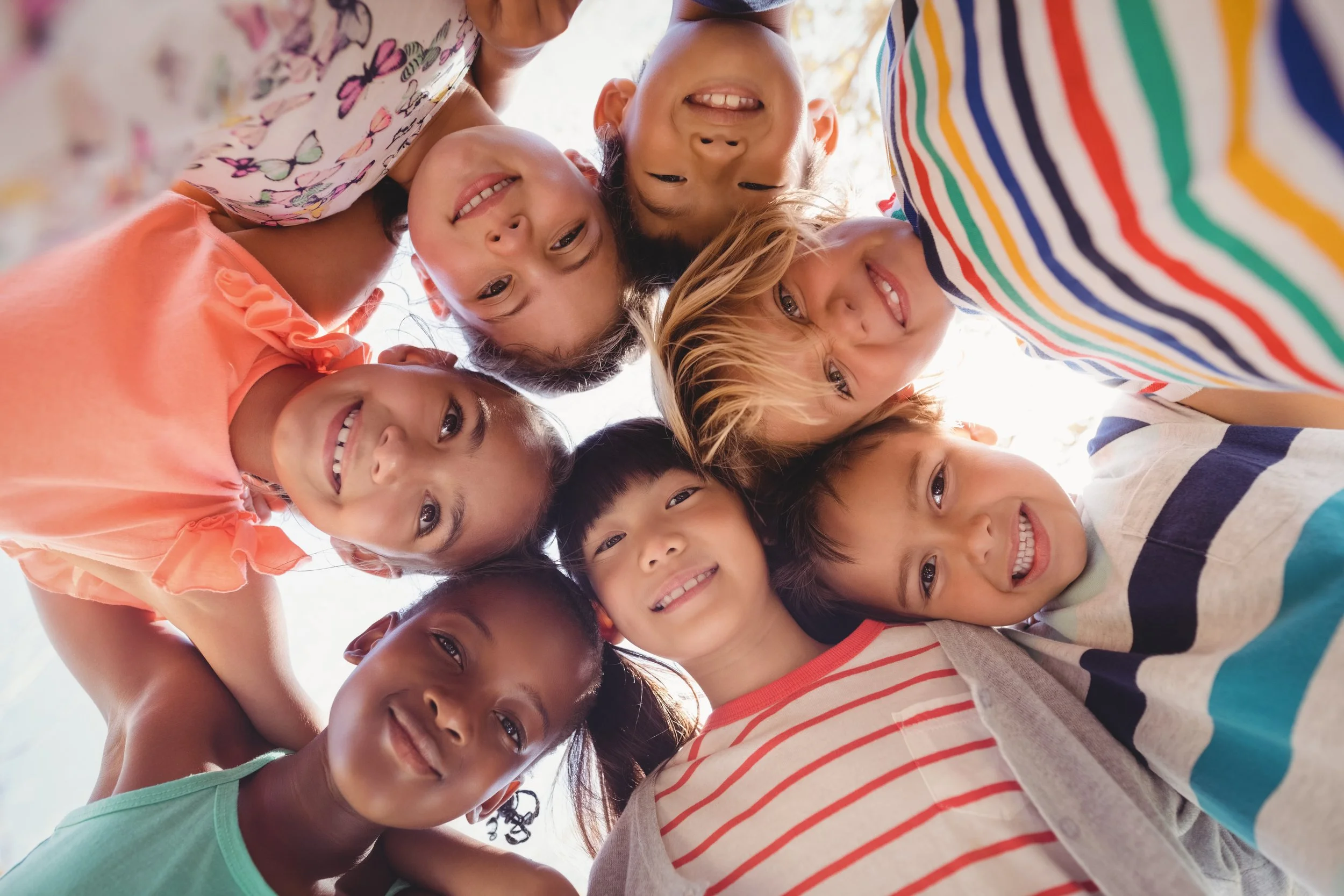 A diverse group of children, smiling and looking down at the camera in a circle