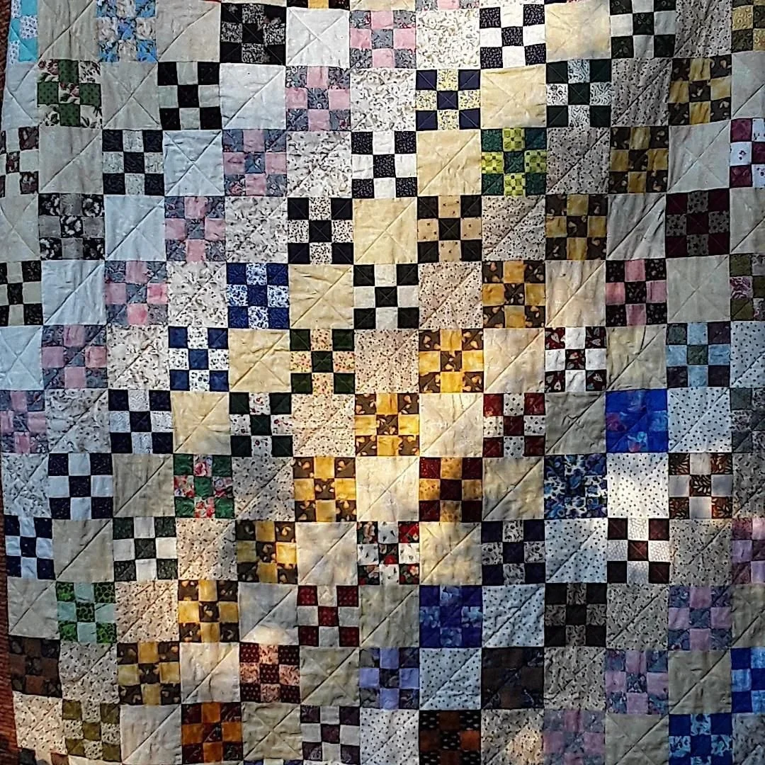 A quilt with a patchwork design of various colorful and patterned fabric squares, arranged in a geometric pattern.