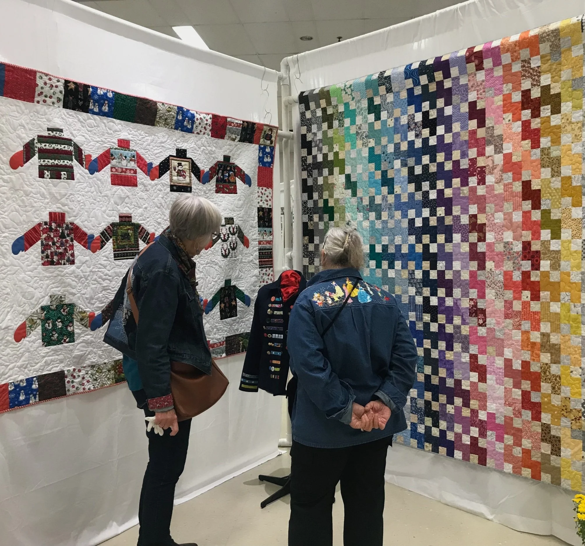 Two women viewing and discussing two large, colorful quilts on display at an exhibition.
