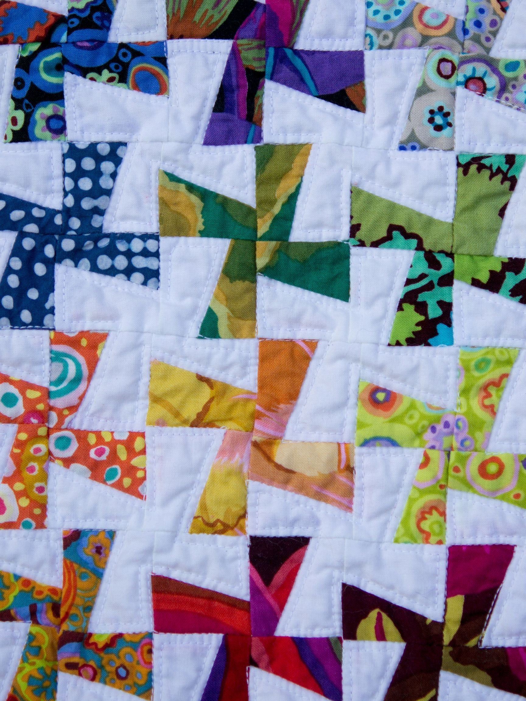 A colorful quilt with geometric patterns, featuring various bright and patterned fabric pieces sewn into a patchwork design.