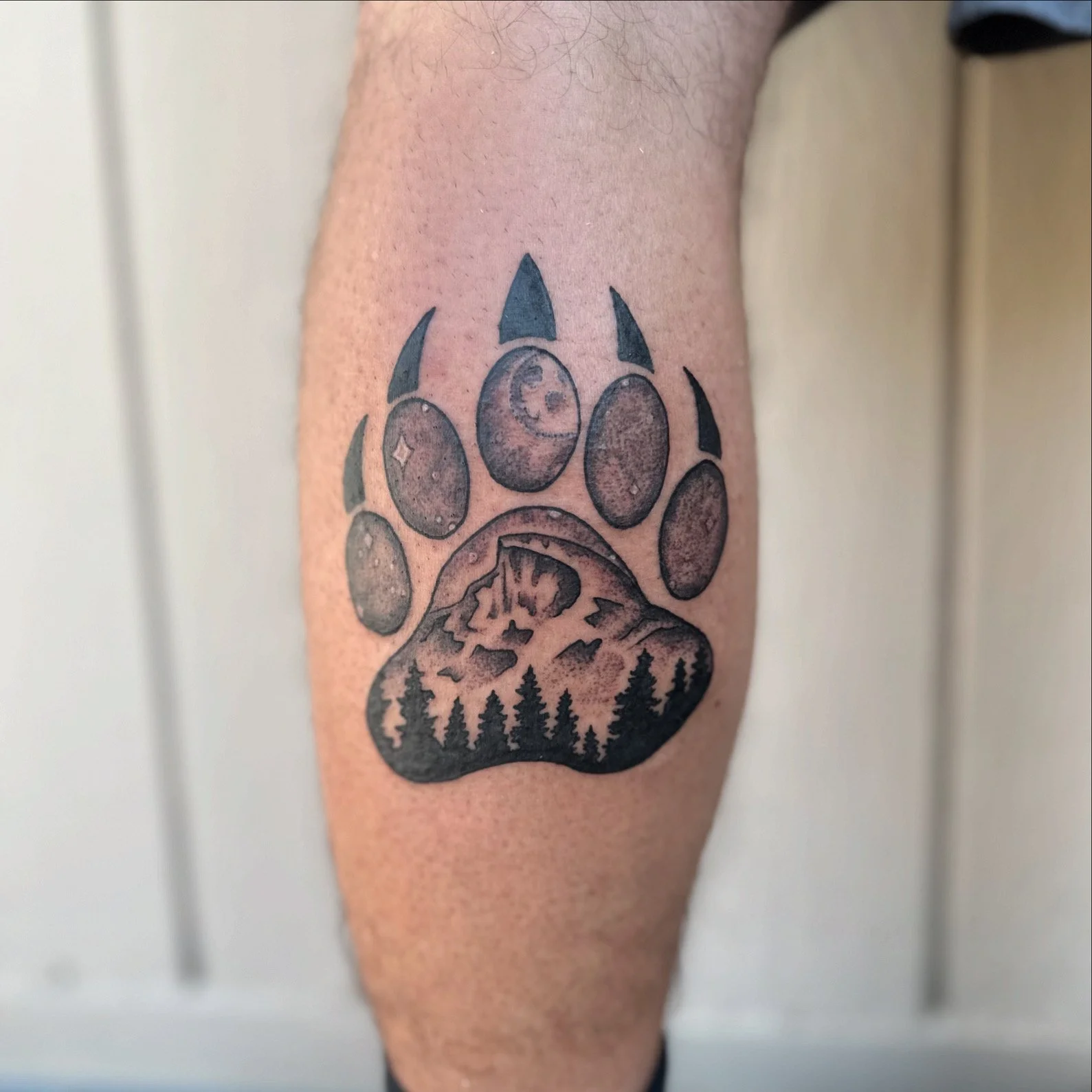 Tattoo of a bear paw with a landscape scene of half dome in Yosemite national park inside the paw on a person's leg.