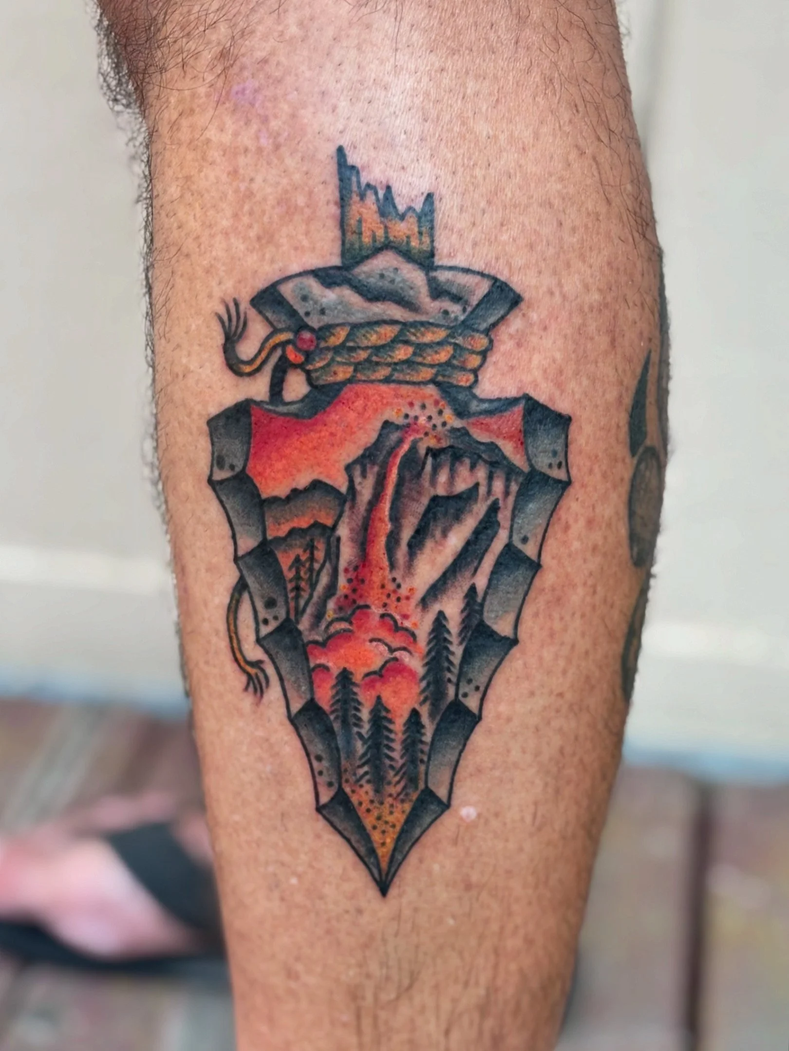 Tattoo of an arrowhead with a mountain scene of Yosemite's firefall, on a person's leg.