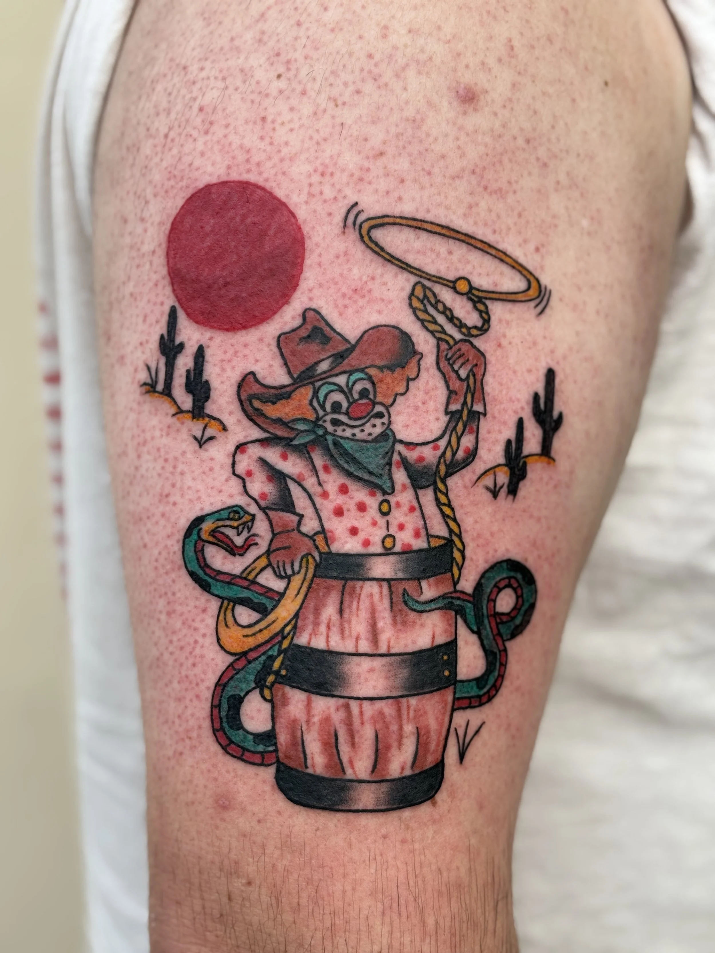 Tattoo of a cartoon cowboy rodeo clown with a red shirt, cowboy hat, and lasso, inside a barrel on a person's upper arm.