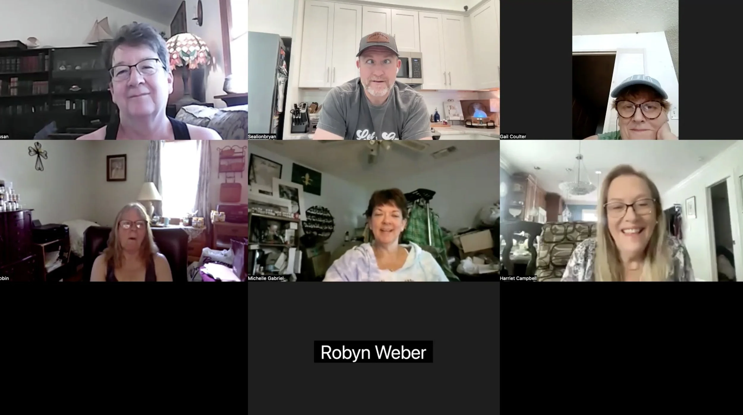 A screenshot of a virtual video call with seven people, six women and one man, in different home settings. Each person is visible in their own square, and they are smiling or looking at their screens.