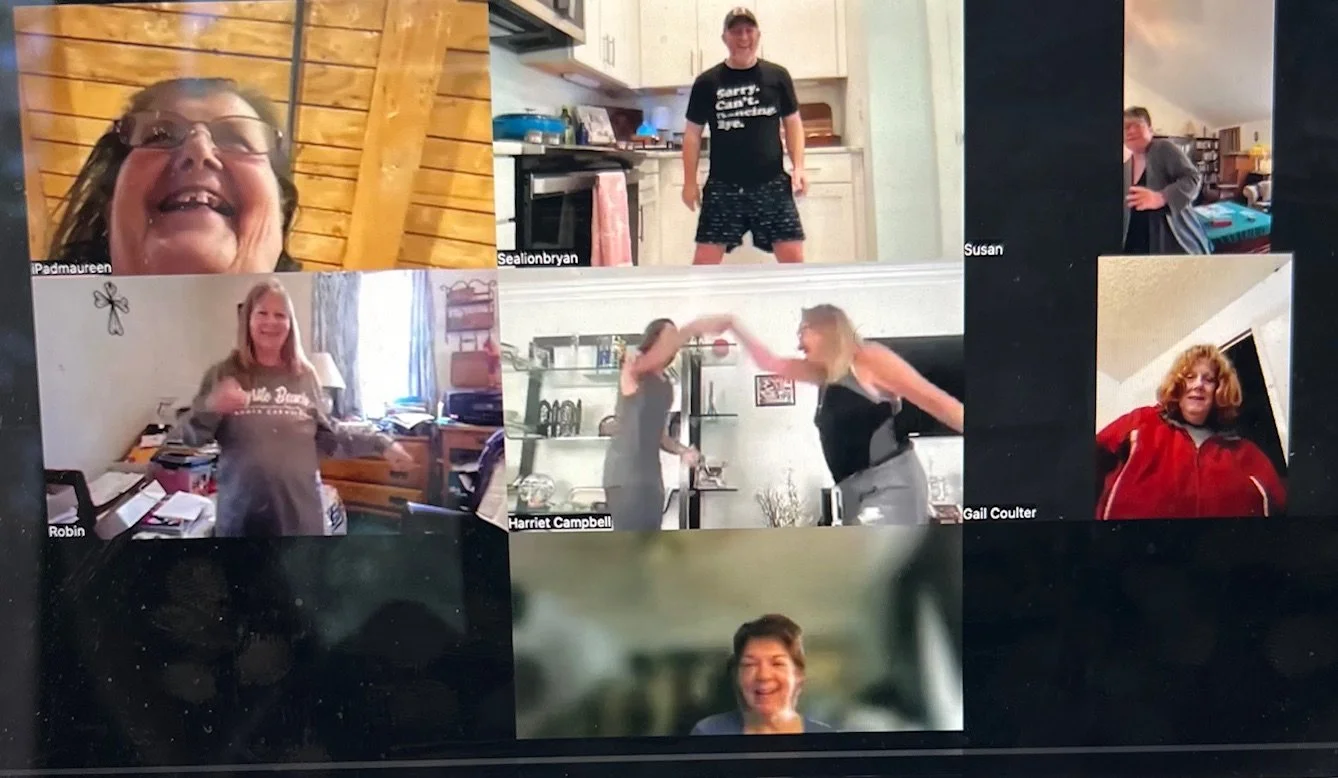 A Zoom call with ten people, some standing and some sitting, in various indoor settings, with one person dancing.