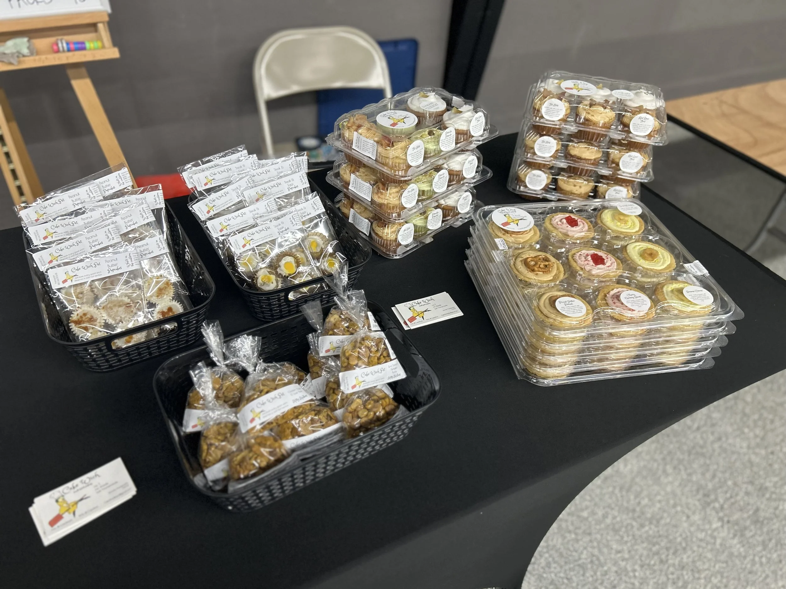 Display of assorted cookies on a table, including individually wrapped cookies, cookies in a plastic container, and decorated cookies with pink and yellow icing.