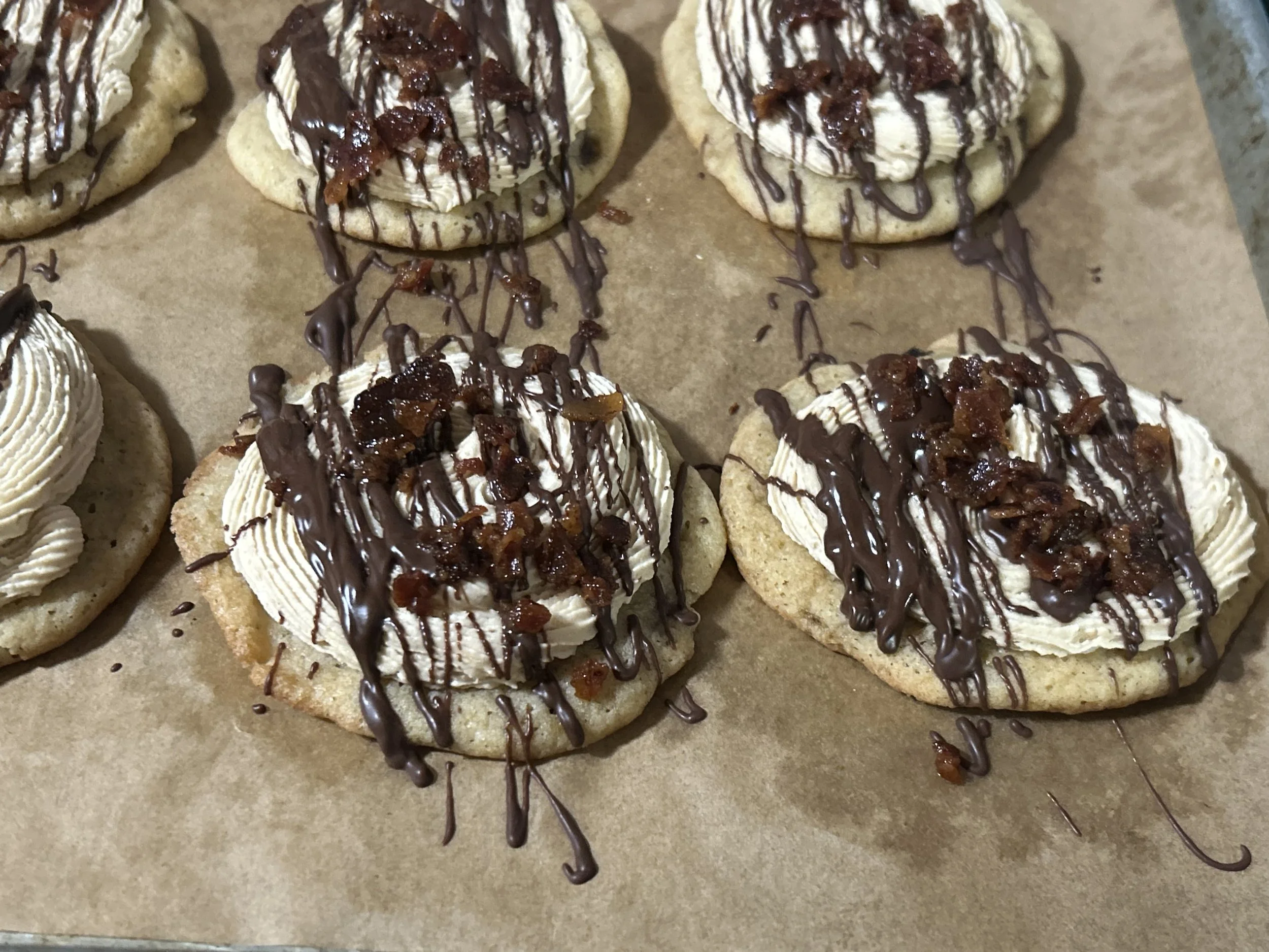Close-up of cookies topped with whipped cream, chocolate drizzle, and caramelized bacon bits.