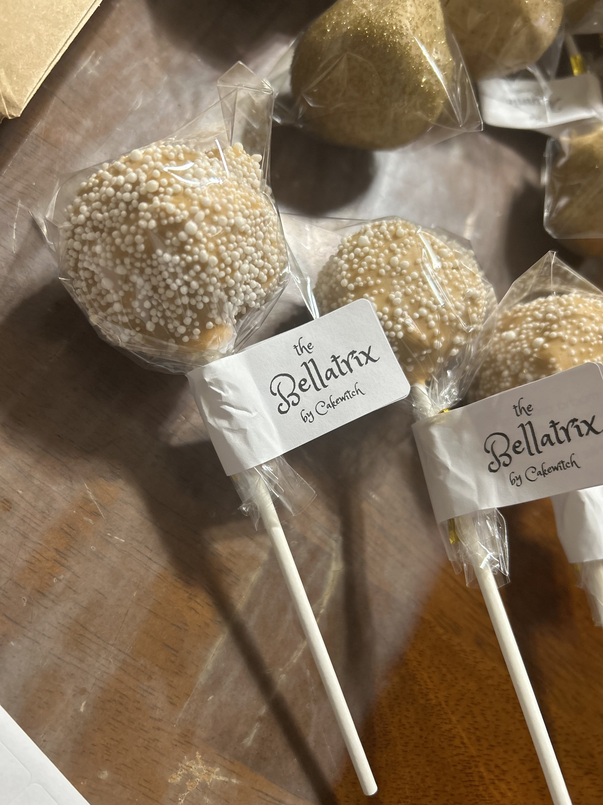 Cotton candy lollipops with white sprinkles, labeled 'the Bellatrix by Cakewitch'