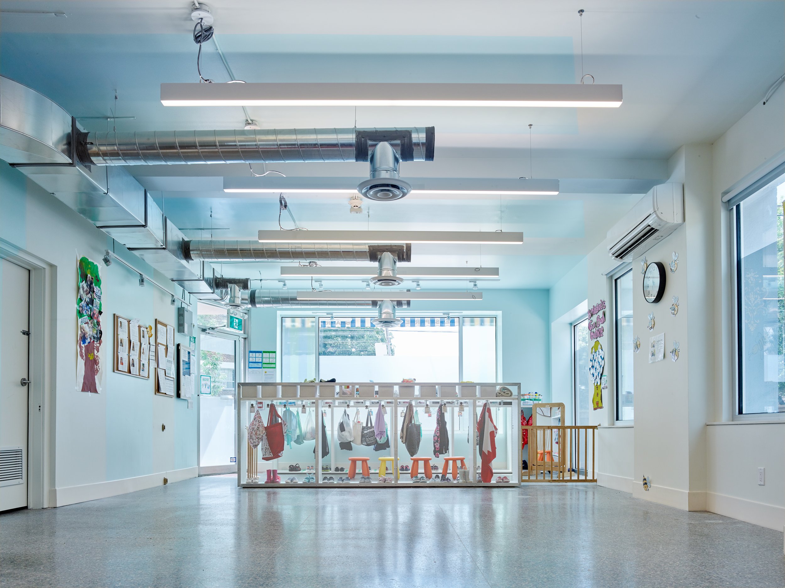 Bright and spacious interior of the Bumble Bee Academy, featuring an open layout with blue-painted ceilings, exposed ductwork, and organized coat racks for children’s belongings.