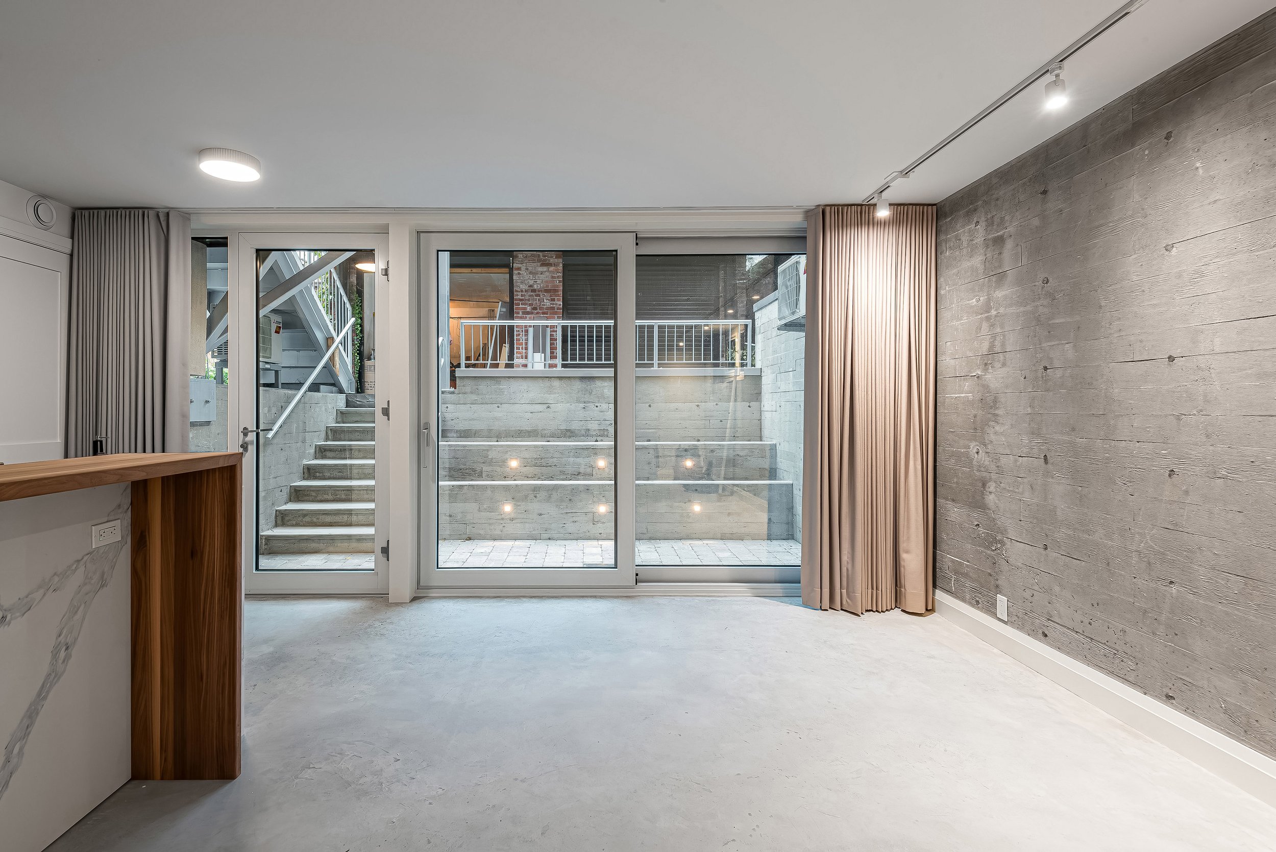 Ground-level suite with floor-to-ceiling glass doors opening to a private walkout courtyard. The raw concrete walls and tiered landscape enhance privacy while integrating natural textures.