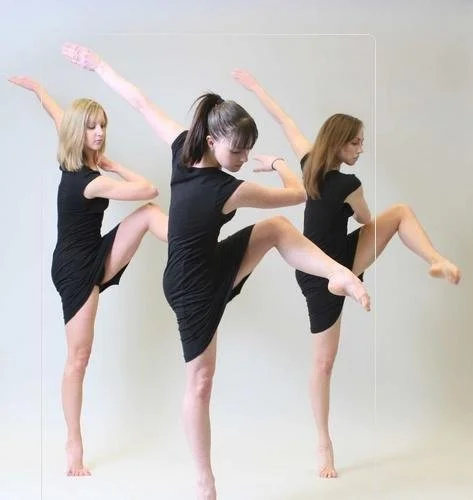 Three women in black dresses practicing ballet poses indoors with neutral background.