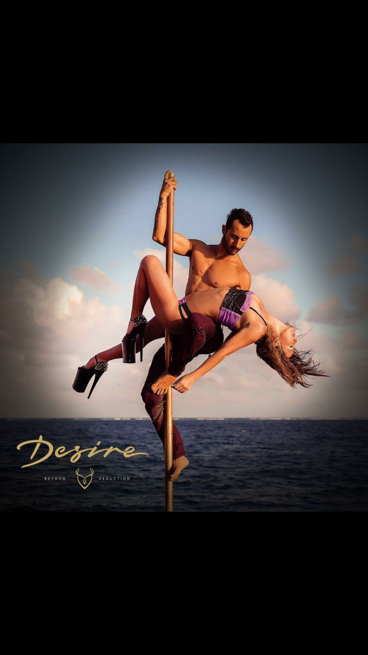 Two people performing a pole dance on a boat with ocean background, featuring stylized text "Desire Beyond Seduction."