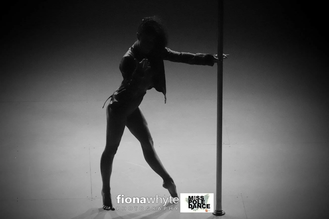 A silhouette of a woman performing a dance move with a pole, standing on one leg with the other bent. She is reaching out with one arm and holding the pole with the other. The background is plain and dark. The image has the text 'fionawhyte PHOTOGRAP