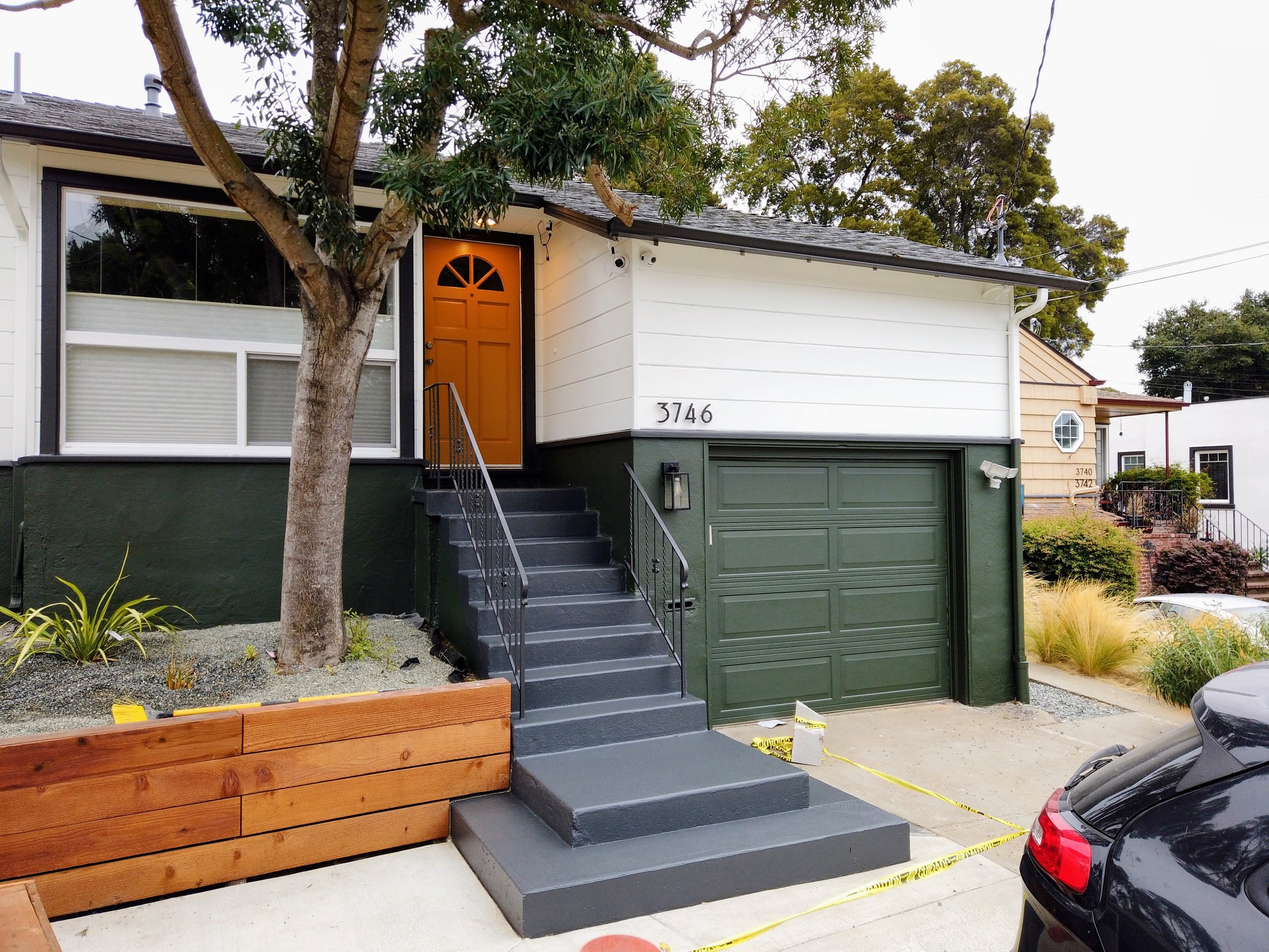 exterior of house where the bottom half is painted green stucco and the top half is wood siding painted white. there is a freshly painted porch and steps leading to a bright and welcoming orange door.