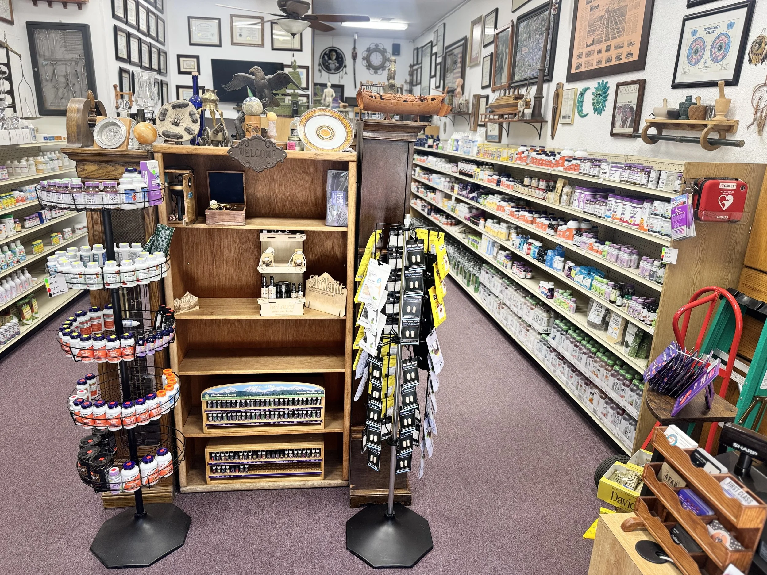 A pharmacy store with shelves filled with medications and health products, and various decorative items on top of the central wooden display, including framed pictures, sculptures, and ceramics.