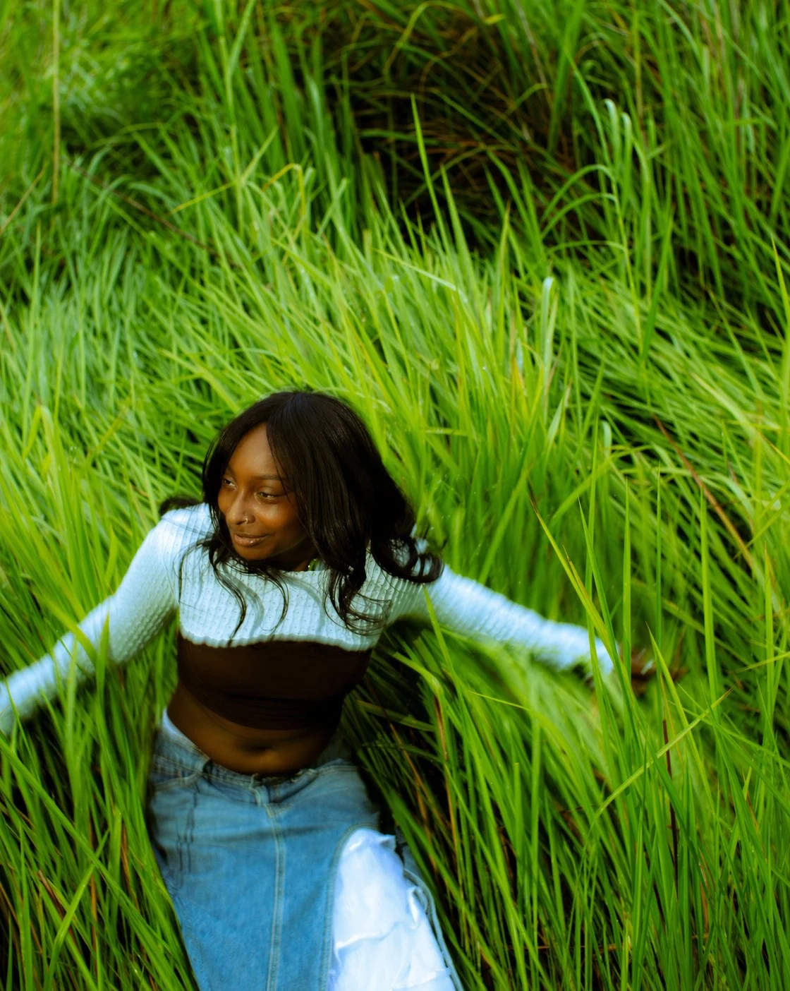Woman sitting among tall green grass in a field.