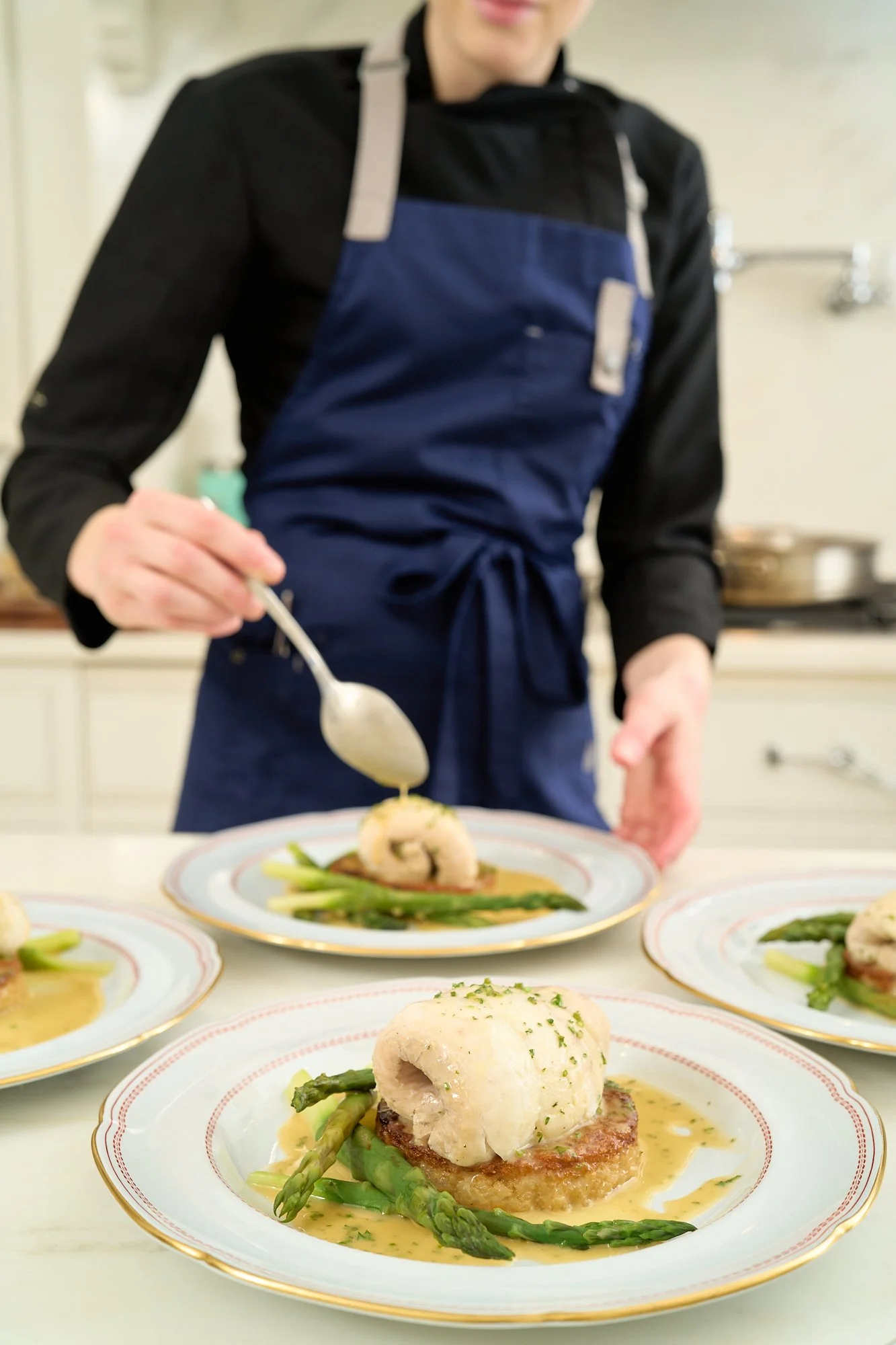 Chef plating a gourmet dish with asparagus and a poached egg on a decorative plate.