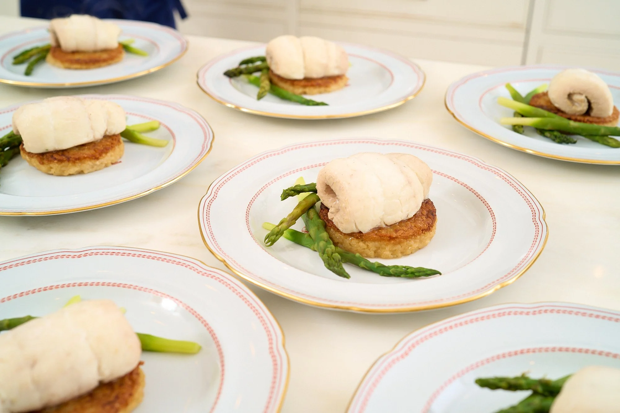 Multiple plates with biscuits, fried chicken patties, and green asparagus on a white table.
