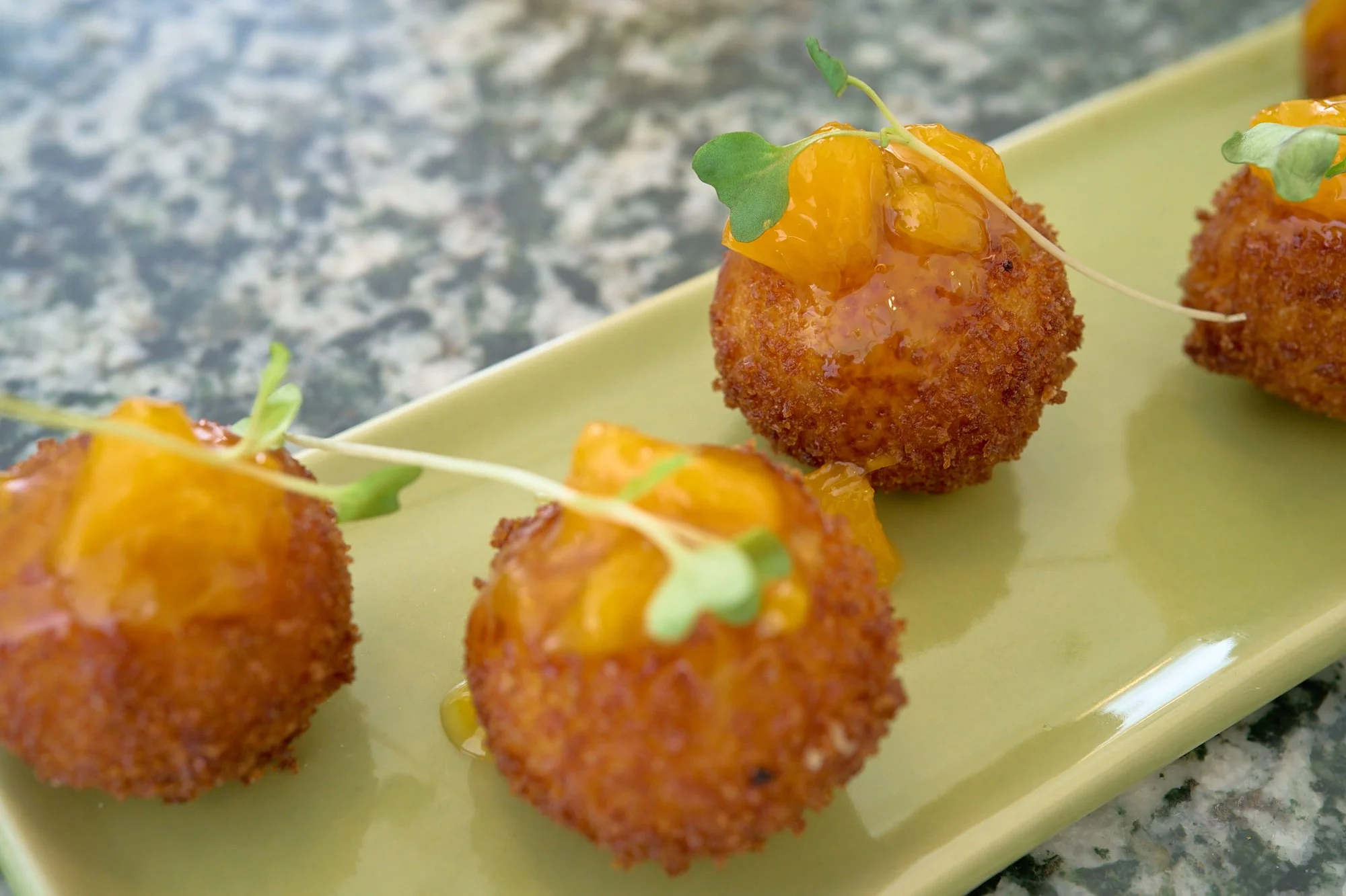 Fried appetizers topped with orange sauce, garnished with microgreens on a yellow platter.