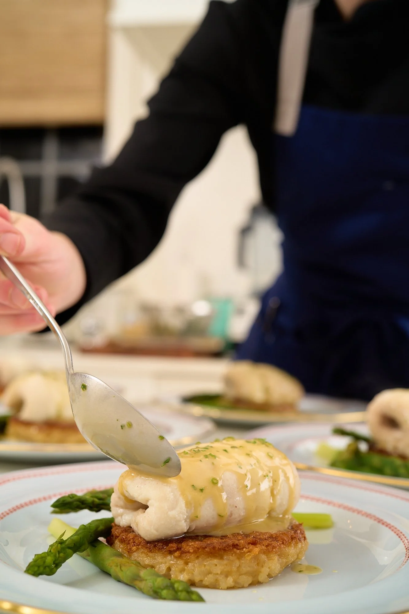 A plated dish featuring a piece of fish topped with a creamy sauce and garnished with herbs, served on a bed of roasted vegetables and asparagus.