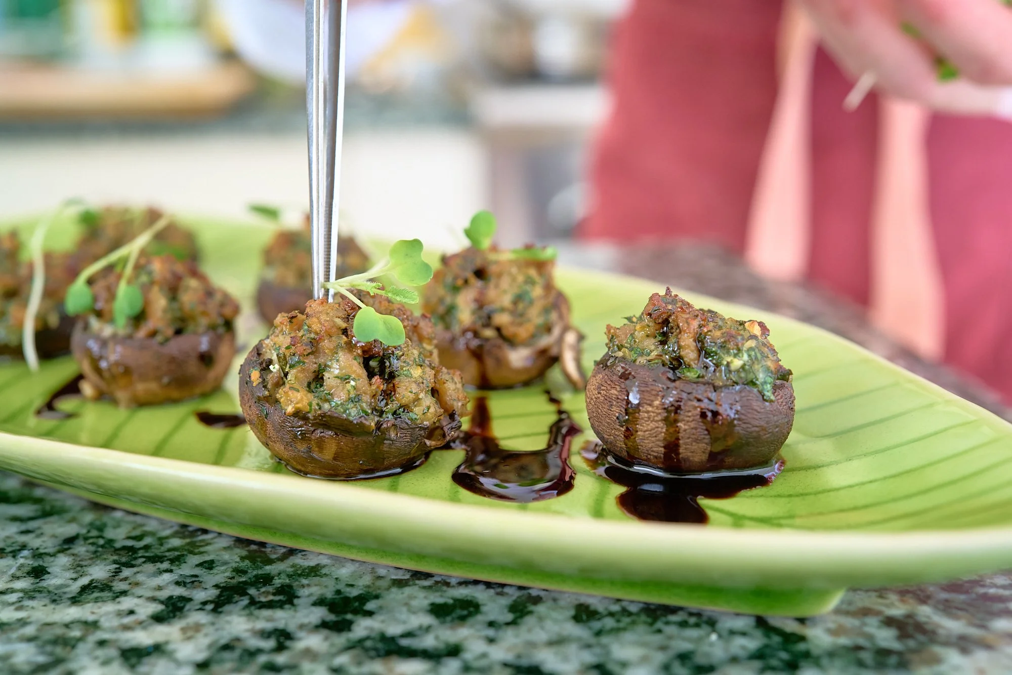 Close-up of stuffed mushroom caps topped with herbs and sauce, served on a green banana leaf.