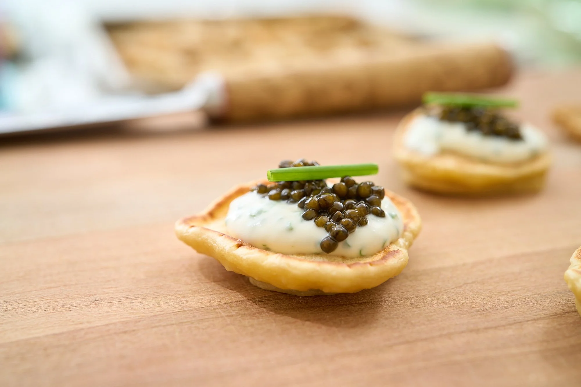 Close-up of a canapé with a spoon of creamy topping, black caviar, and a green garnish on a pastry cup.