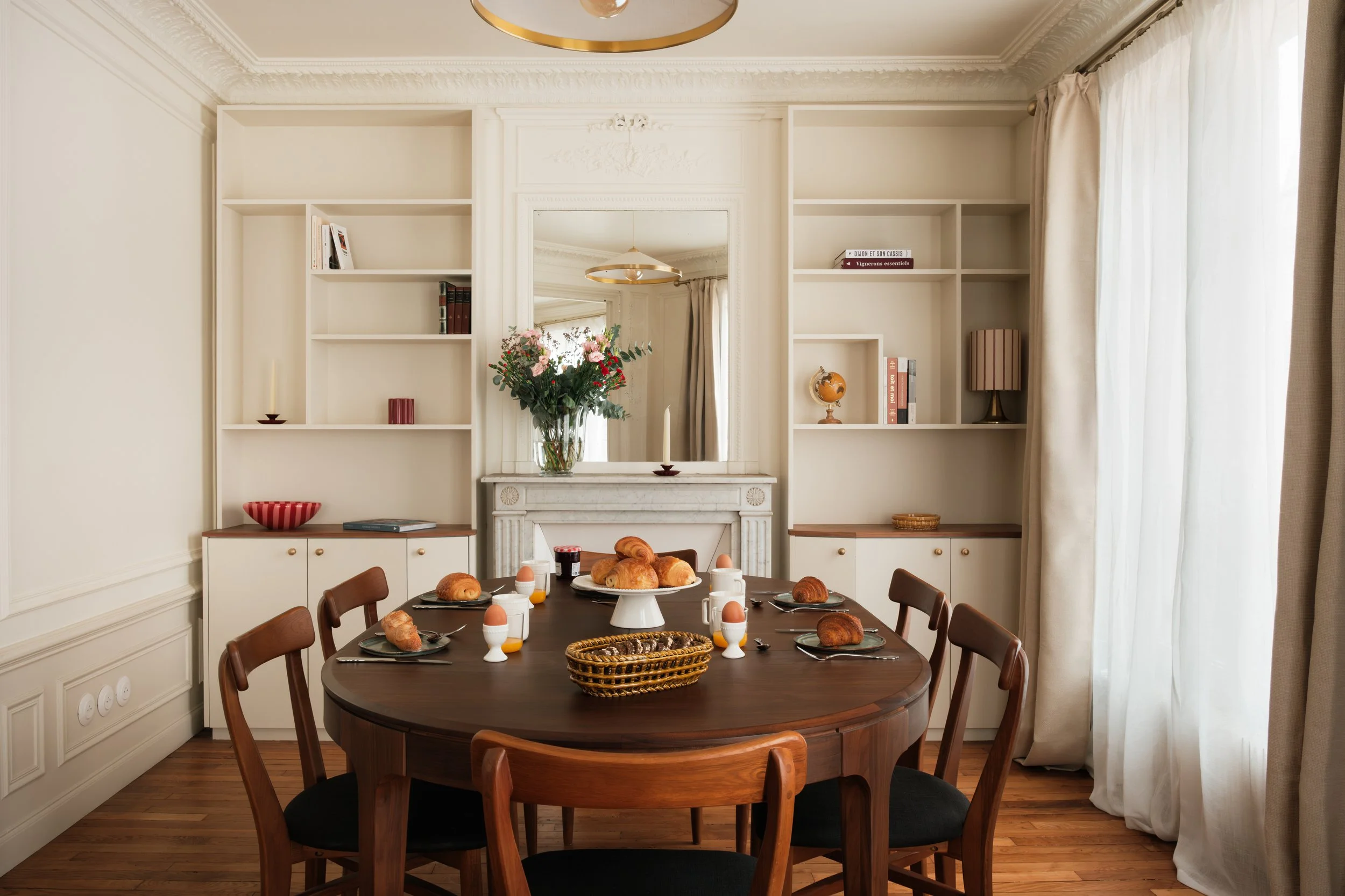 Salle à manger dans appartement Haussmannien haut de gamme avec bibliothèque sur mesure et table en bois.