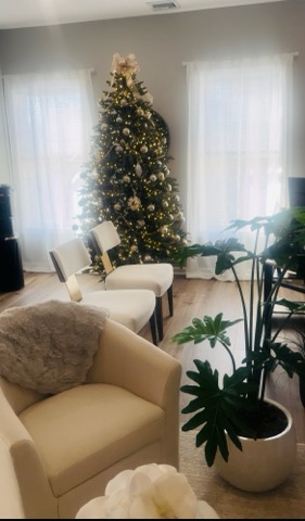 Decorated Christmas tree with gold ornaments and lights in a living room with white curtains and furniture.