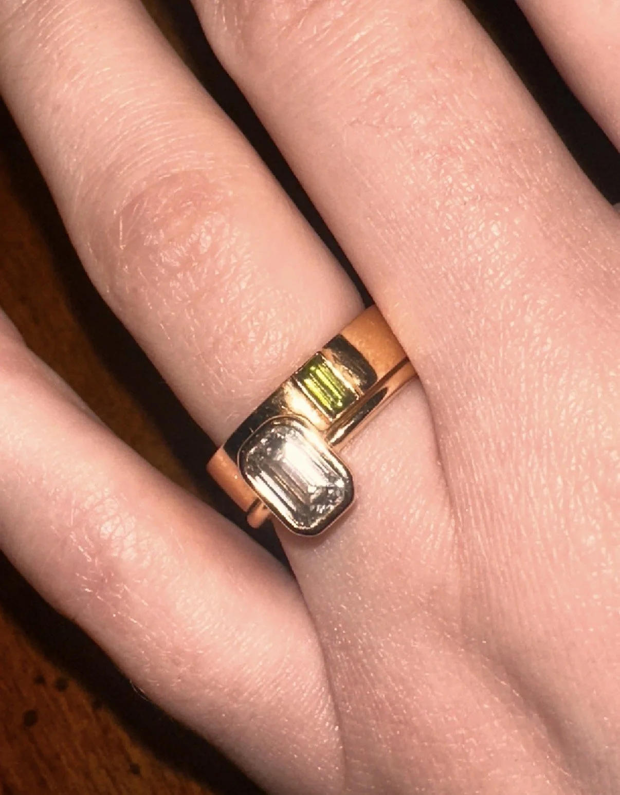 Close-up of a hand wearing a yellow gold engagement ring with a large emerald cut diamond and baguette tourmaline on the wedding band.