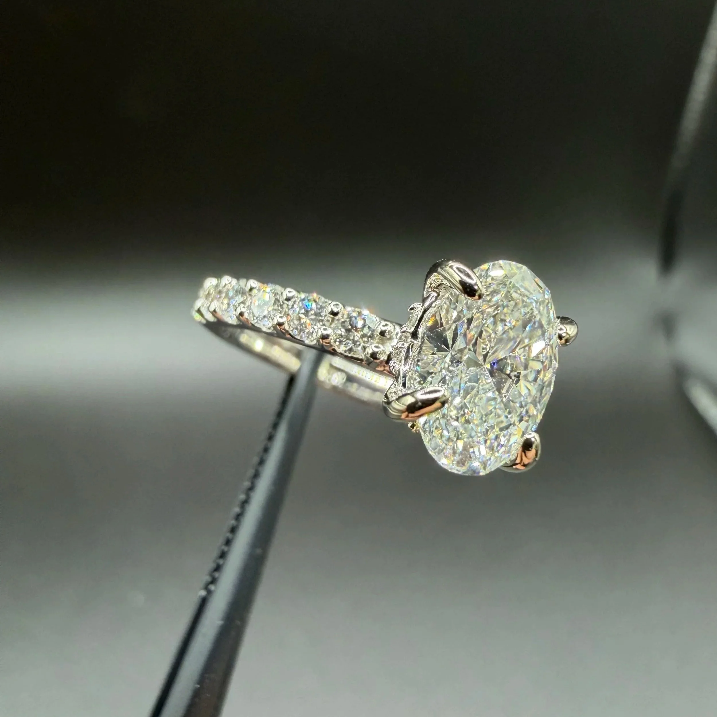 Close-up of a silver ring with a large heart-shaped diamond and smaller diamonds on the band, displayed on a metallic stand.