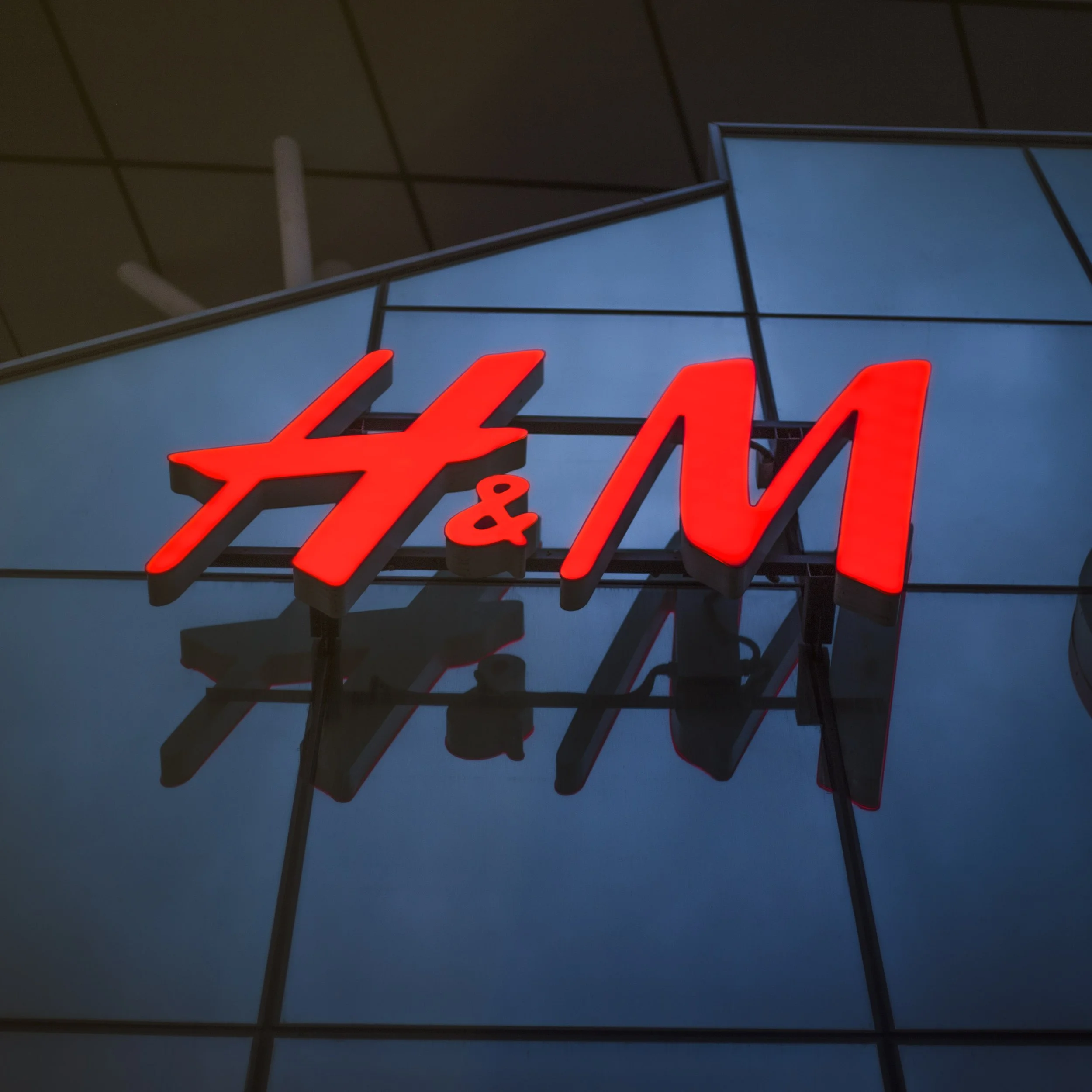 Logo de H&M en una fachada de cristal iluminada en color rojo.