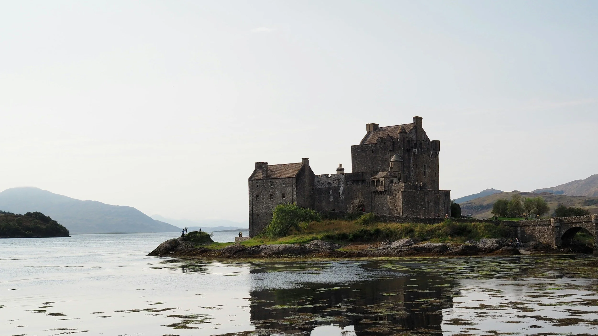 A historic castle on a small island surrounded by water with mountains in the background.