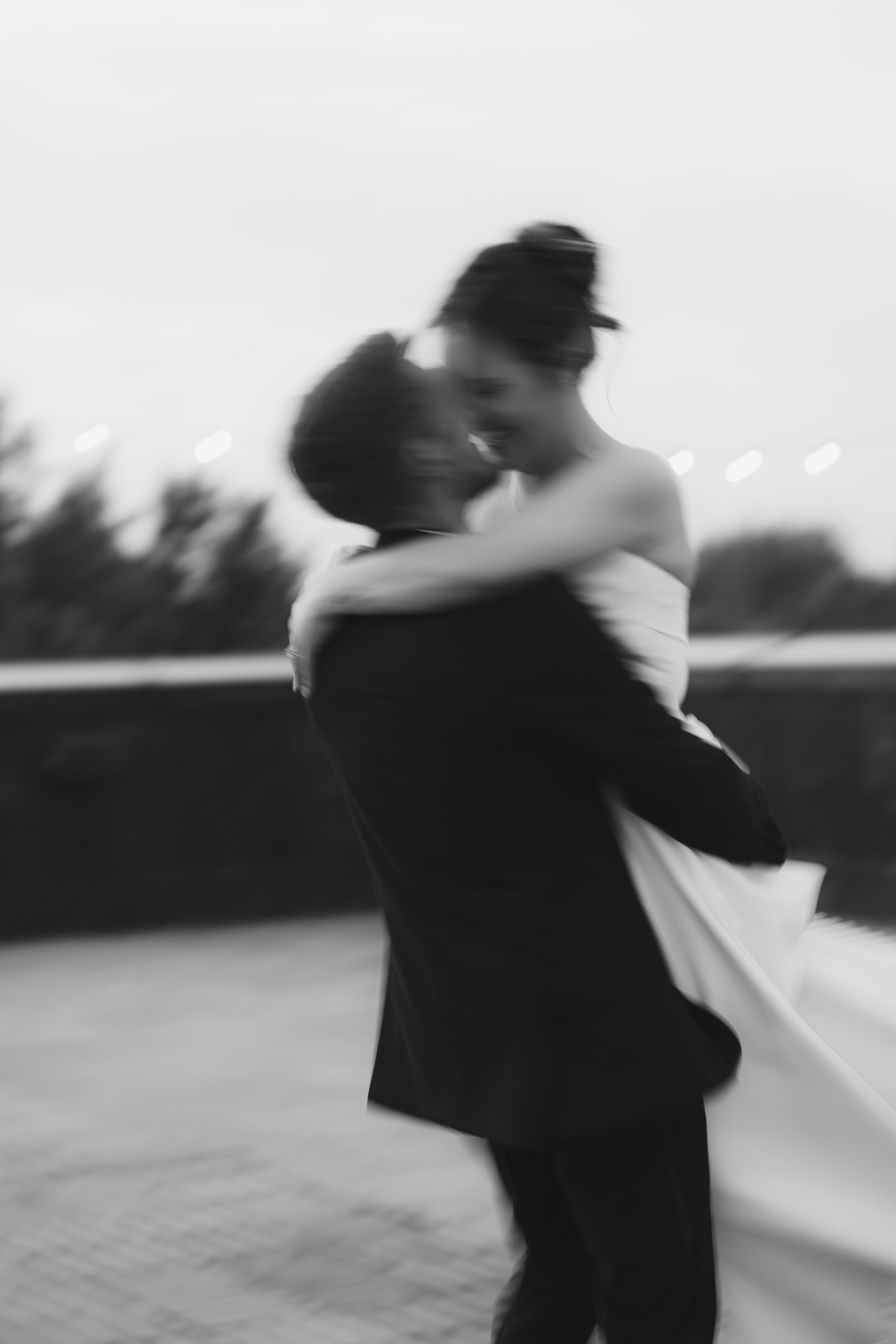 Blurred black and white image of a person dancing outdoors, with their eyes closed and arms crossed.