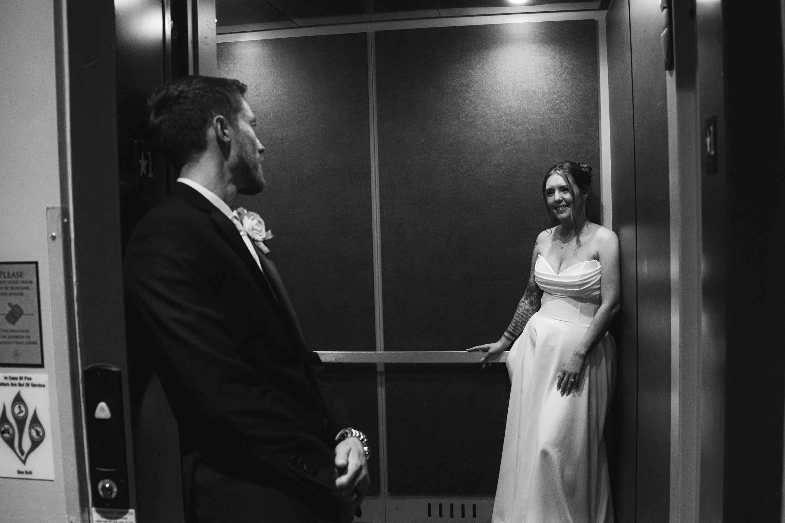 A man and woman in an elevator, with the woman sitting on a bench and smiling at the man.