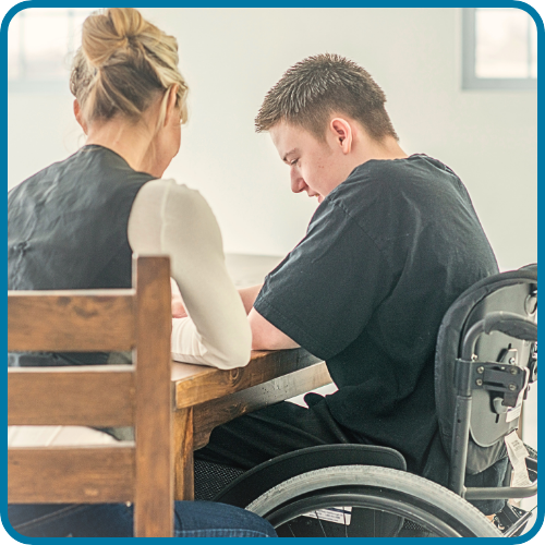 A young man in a wheelchair and a woman sitting at a table, engaging in a conversation.