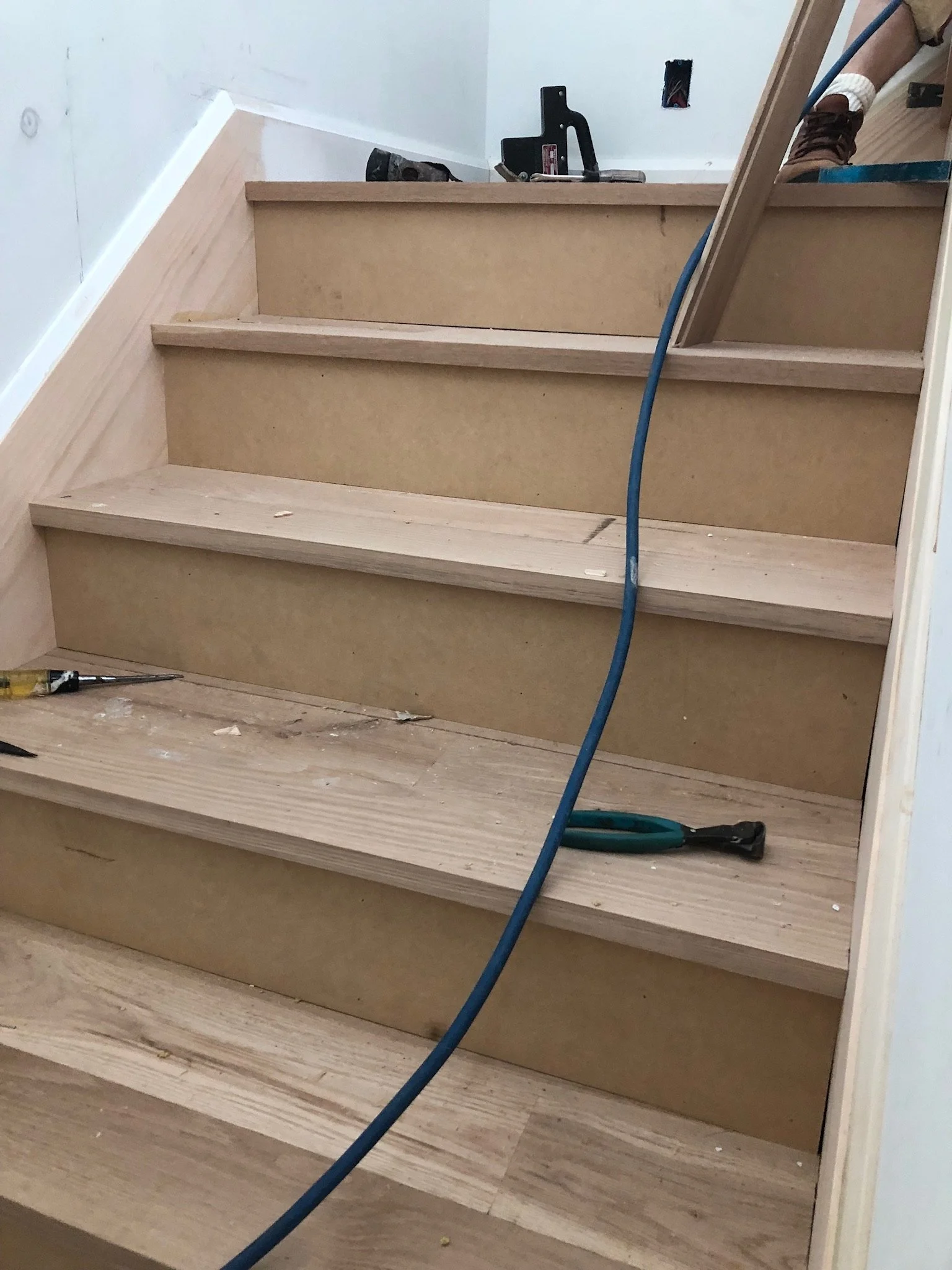 Partially constructed staircase with tools and blue air hose.