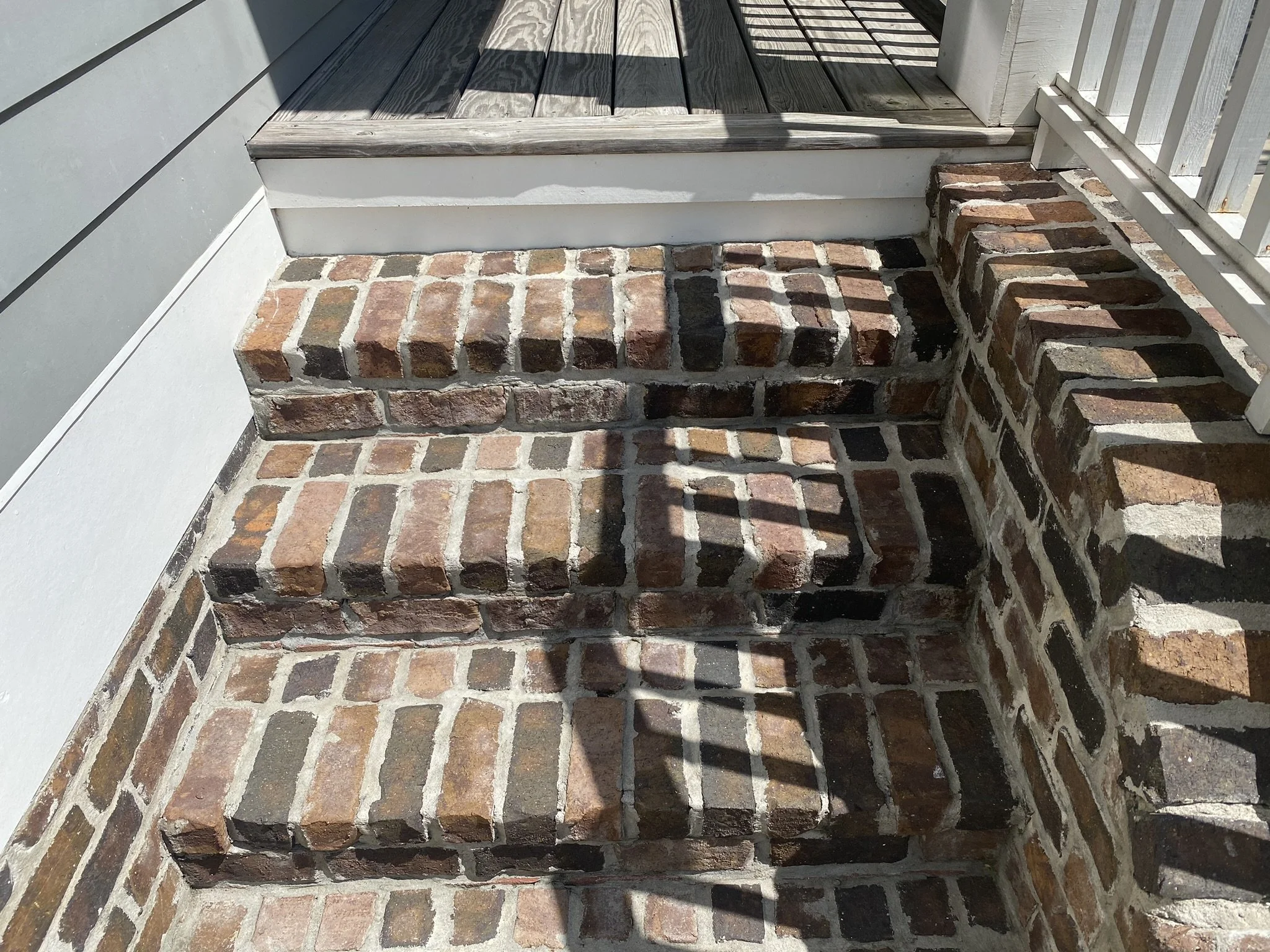 Brick steps leading up to a wooden porch with light shadow patterns.