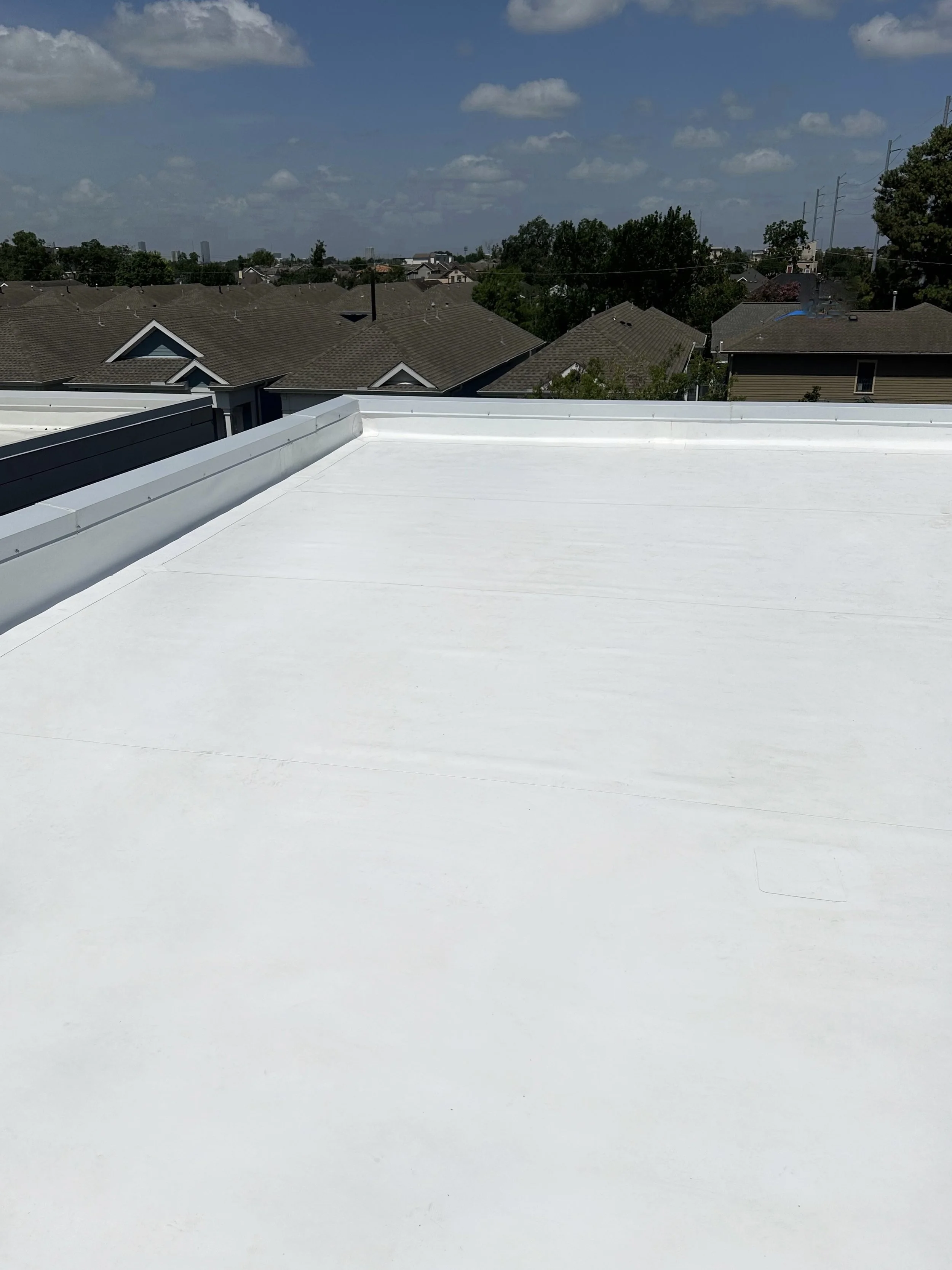 White flat roof with neighborhood and trees in background under a cloudy sky.