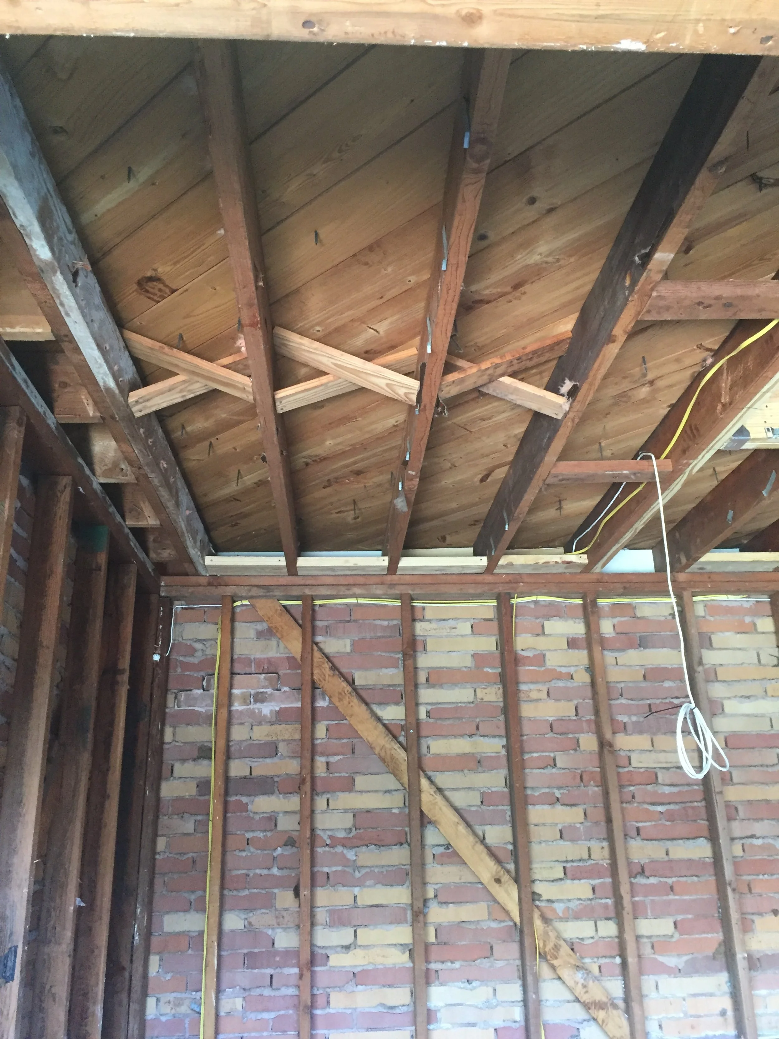 Exposed wooden roof rafters and brick wall in a partially constructed building interior.