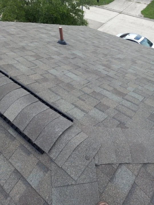 Asphalt shingle roof with a vent pipe and ridge vent in a residential area.