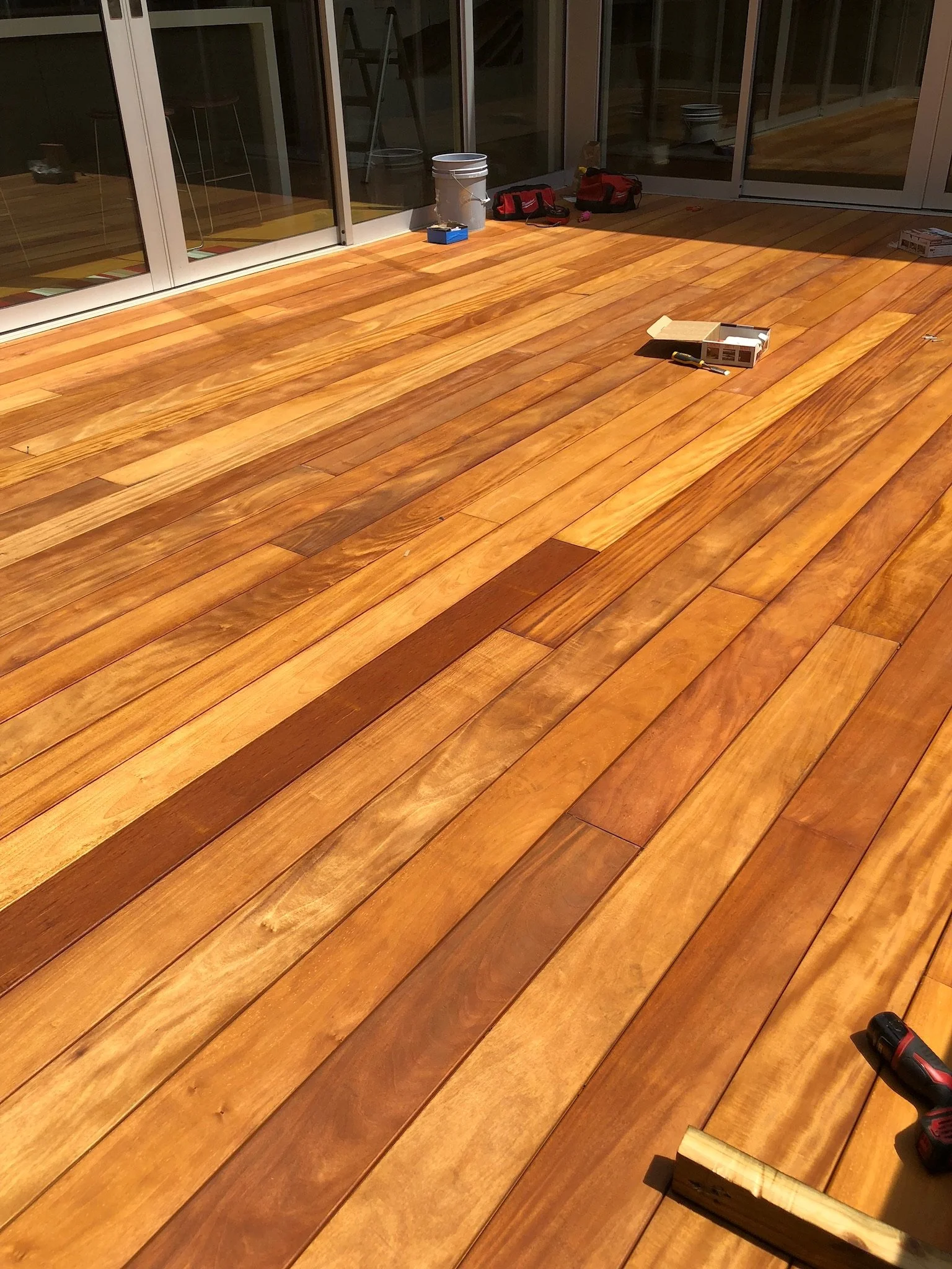 Wooden deck with tools and a paint bucket near sliding glass doors