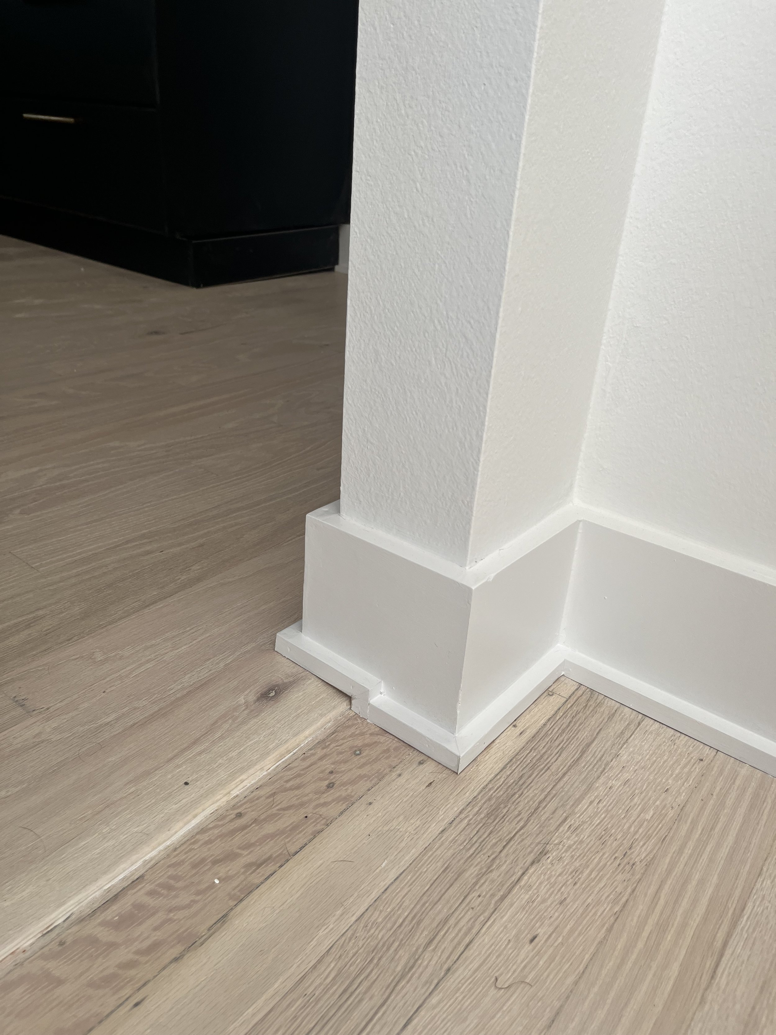 Corner of a room with white baseboards and hardwood flooring
